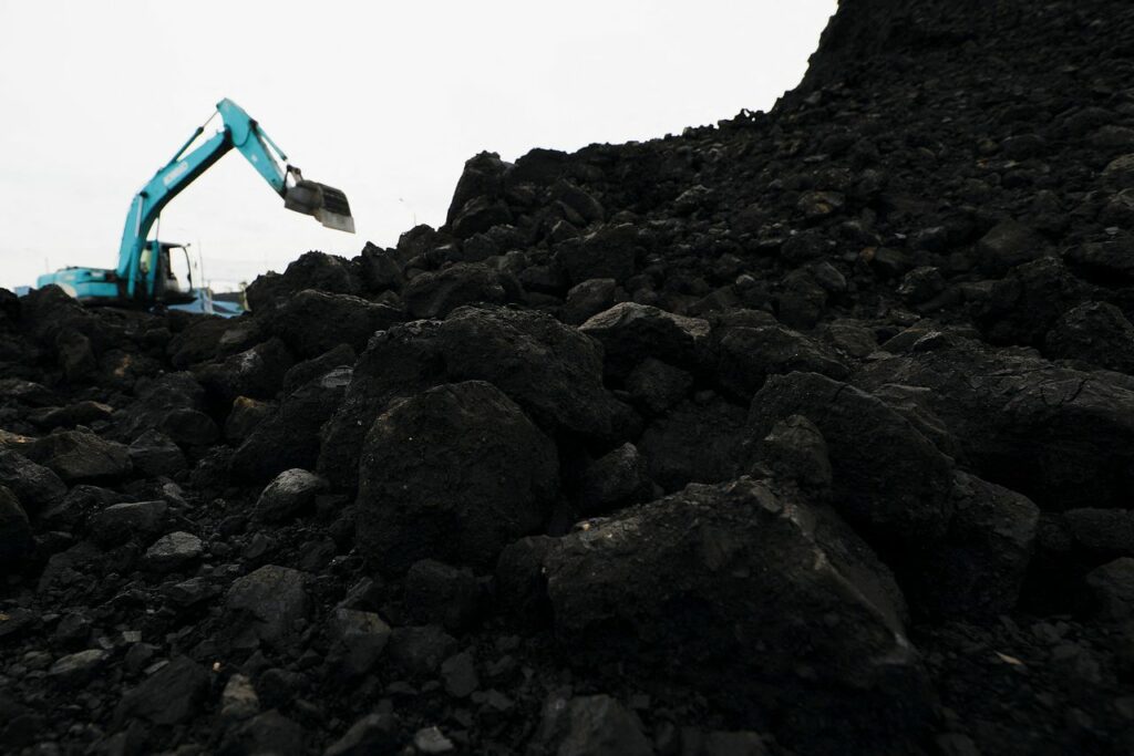 A digger works through a pile of blackened earth