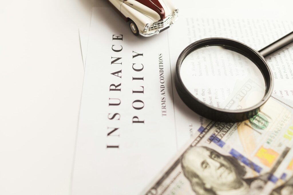 Insurance policy papers with money, a magnifying glass and a model car