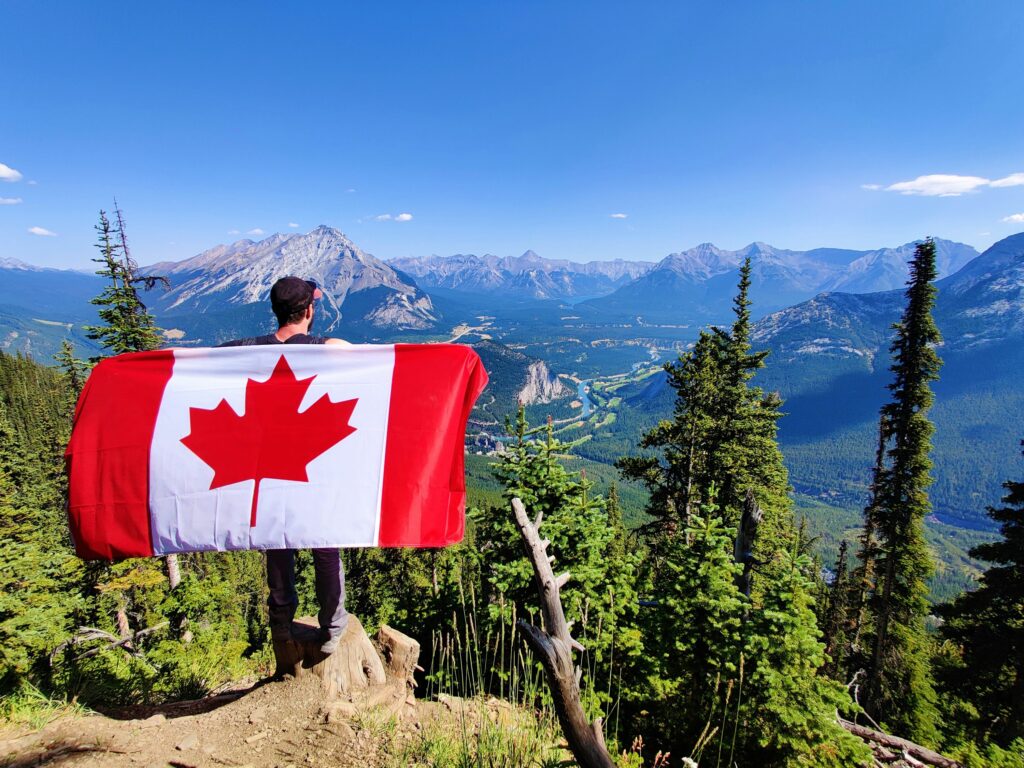 Man holding up the Canadian flag while on a hike in the mountains